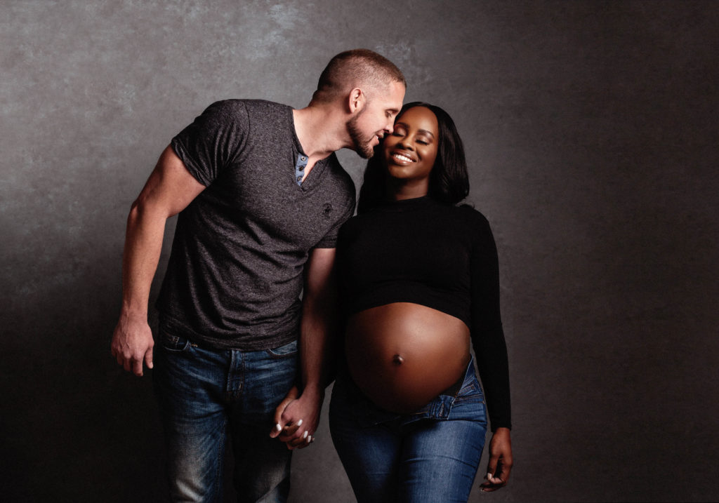 expectant husband and wife hold hands and smile during pregnancy photography photoshoot