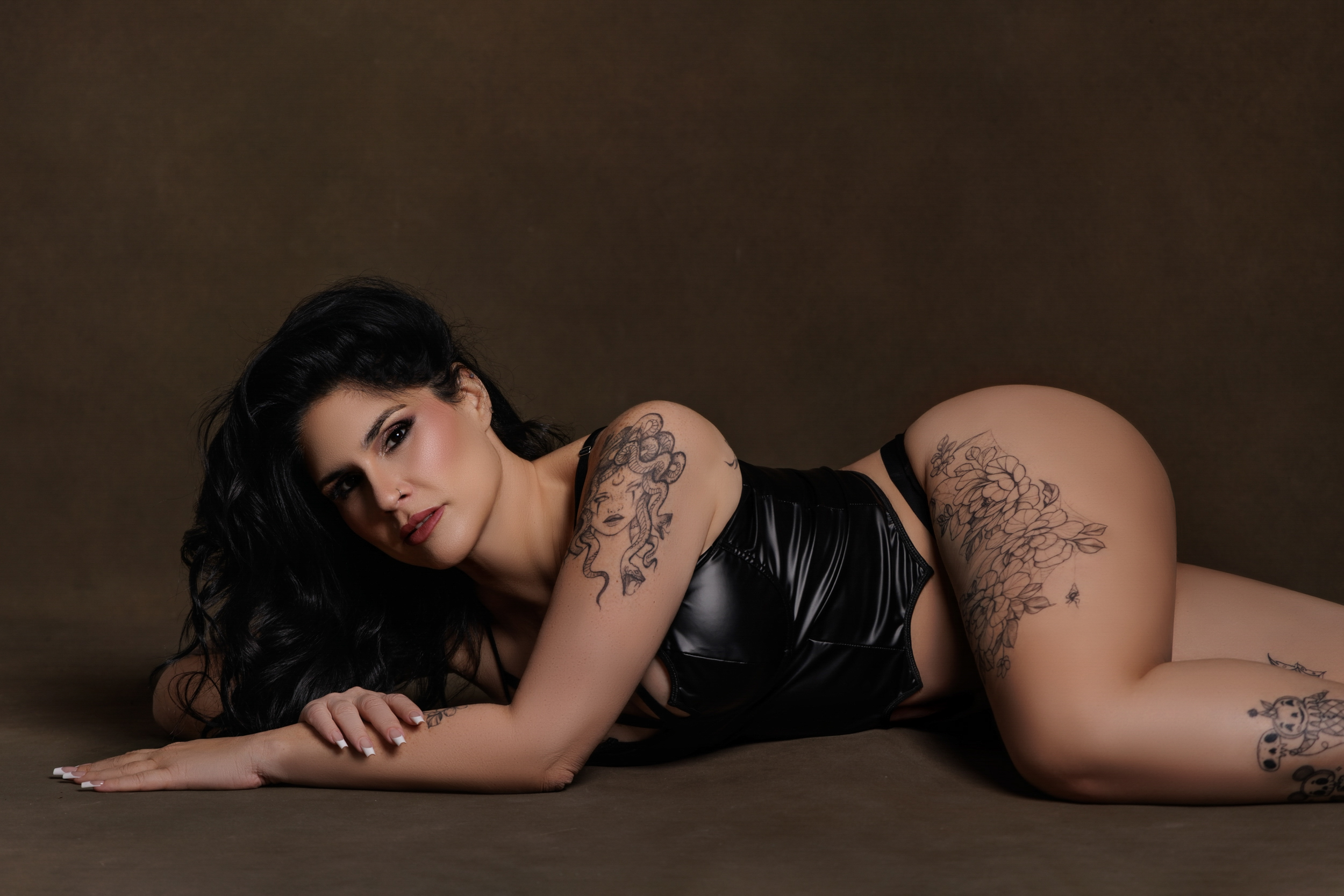 Woman lying on her side on the studio floor wearing black lingerie, photographed in a boudoir portrait with soft lighting in South Florida
