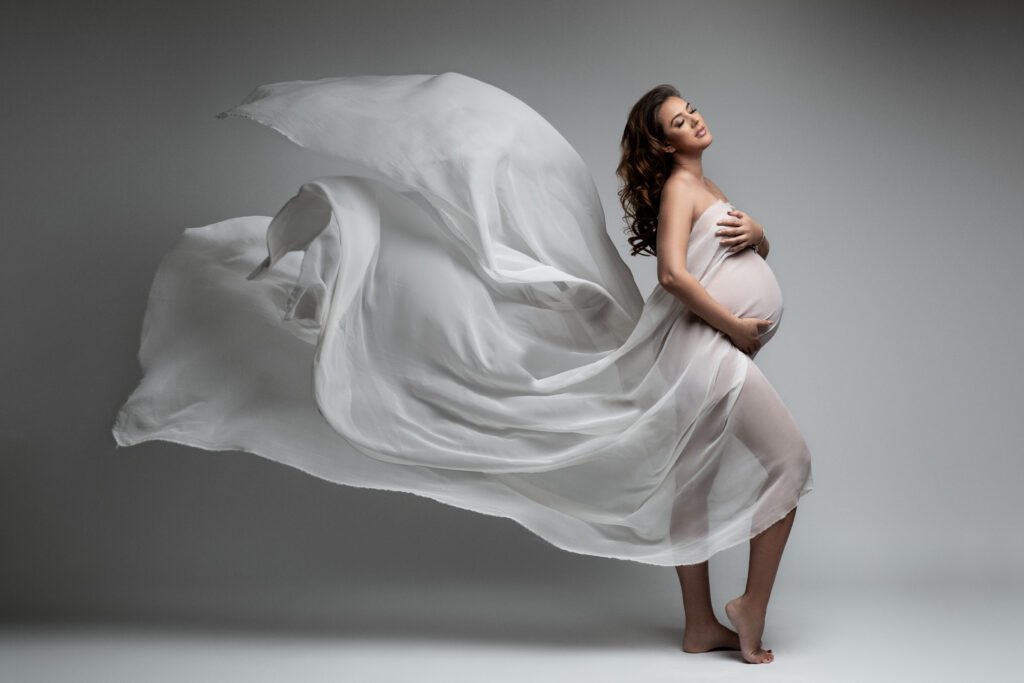 Pregnant woman in flowing white fabric gown during studio maternity photography session