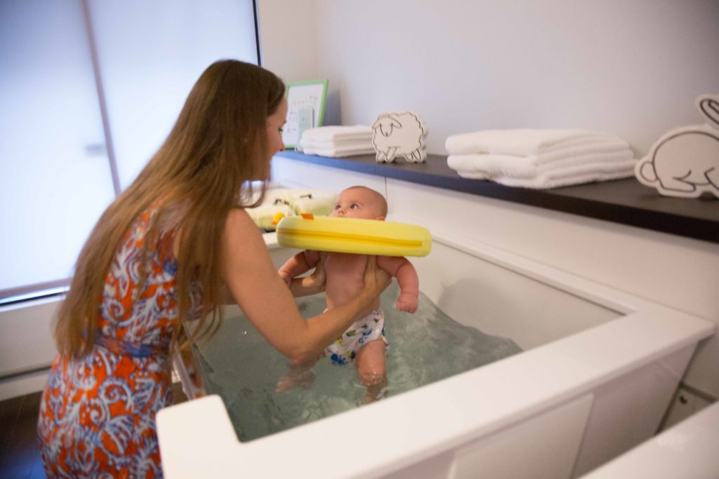 Baby Spa at Amazing Births and Beyond- Woman in Paisley dress holding baby in float barely out of baby spa with yellow float