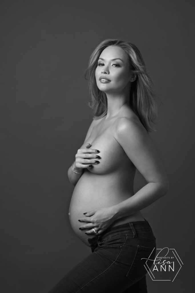 nude pregnant woman in jeans covering breast with hand