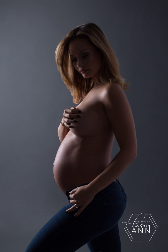 nude pregnant woman wearing jeans looking down with face in shadow