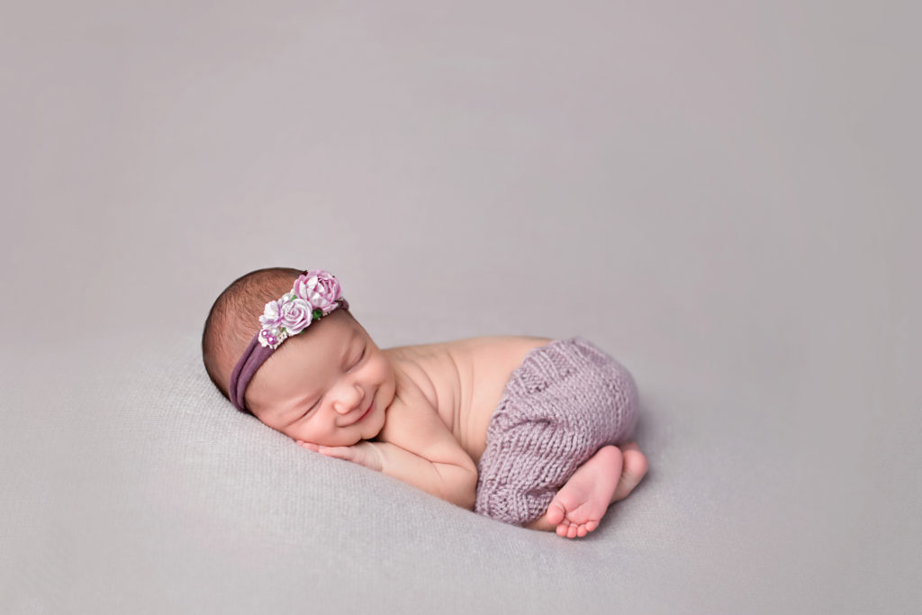 smiling baby girl with purple flower headband and purple shorts