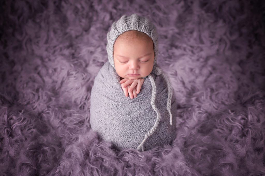 newborn baby photo with purple furry background and gray wrap and grey bonnett.  potato sack newborn pose