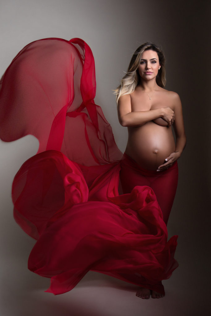 pregnant maternity photograpahy shoot model stands nude with billowing red silk surrounding her.