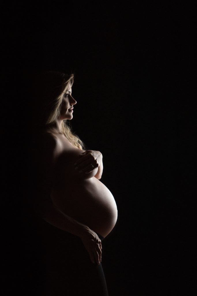 color image of maternity photography shoot with nude model covering her breasts as she looks in profile at the future.