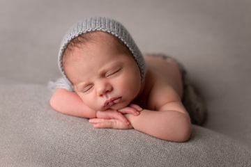 newborn in light blue knit cap sleeping with chin on hands