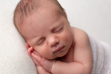 newbornn sleeping with cheeck resting on folded hands, white background