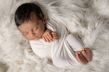 newborn photographed swaddled in a white fabric, lying on a white fur rug