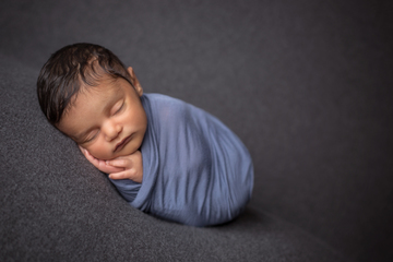 color photograph of newborn swaddled in blue fabric sleeping peacefully