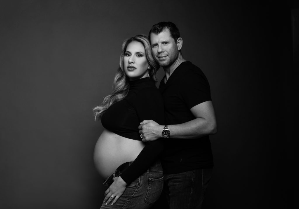 Husband and wife pose in black and white maternity photo with black shirts and jeans