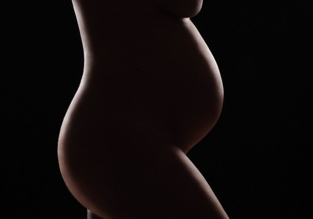 Precious baby bump with silhouette against black background during maternity photoshoot