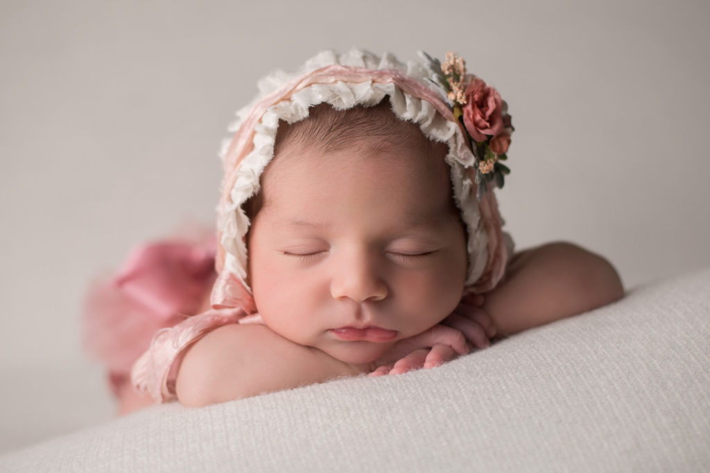 newborn baby girl with floral pastel headband in pink dress on a white blanket