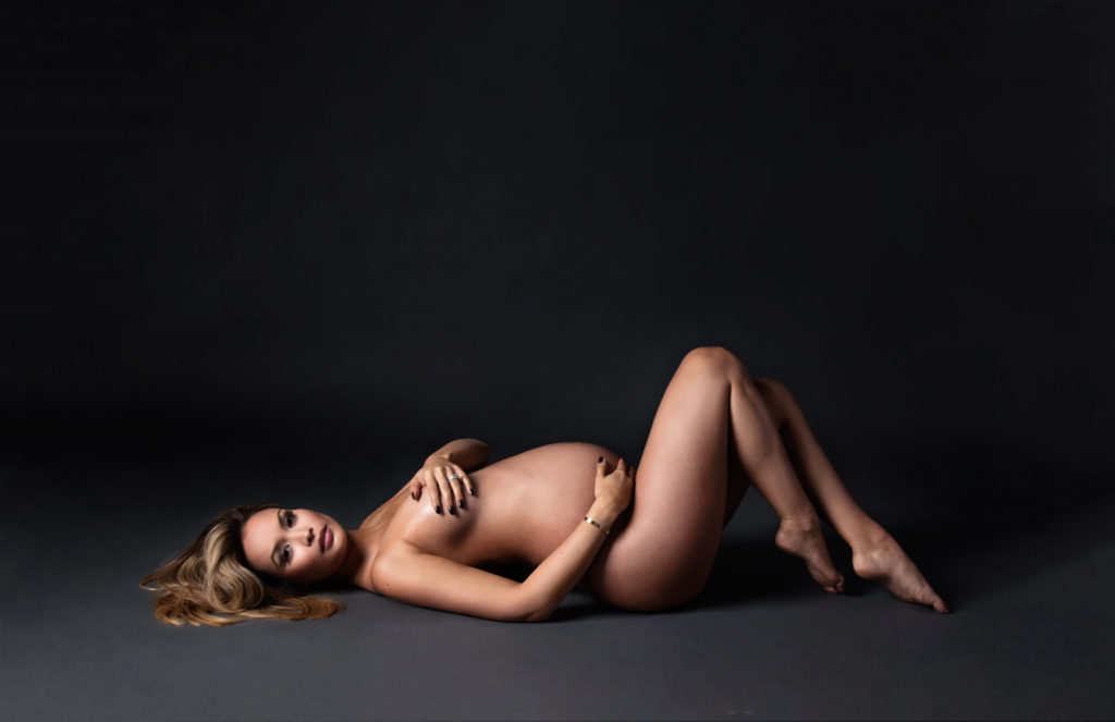 Pregnant mother laying down on back and pointing toes in nude maternity photoshoot