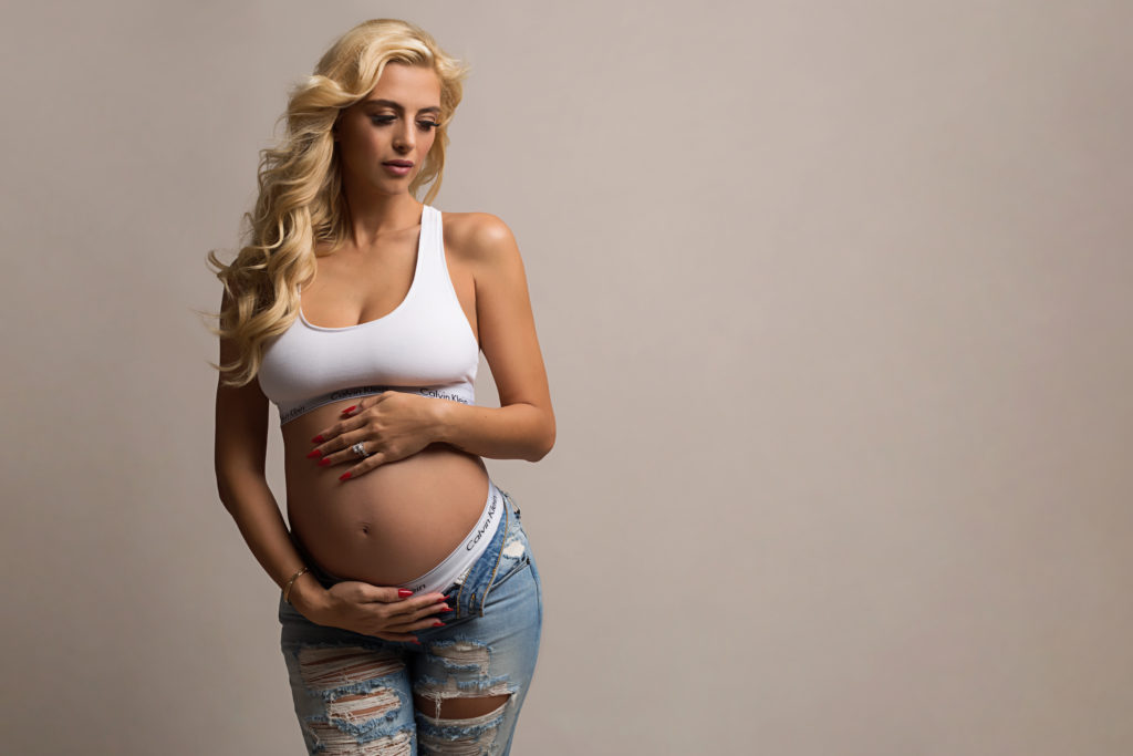 Pregnant mom holds baby bump while wearing jeans and Calvin Klein in maternity photography