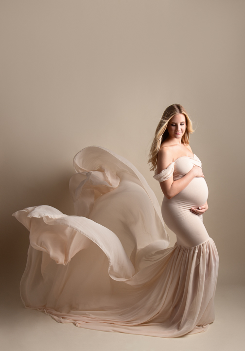 Pregnant woman wearing a tan floor length gown flowing behind her in maternity photoshoot