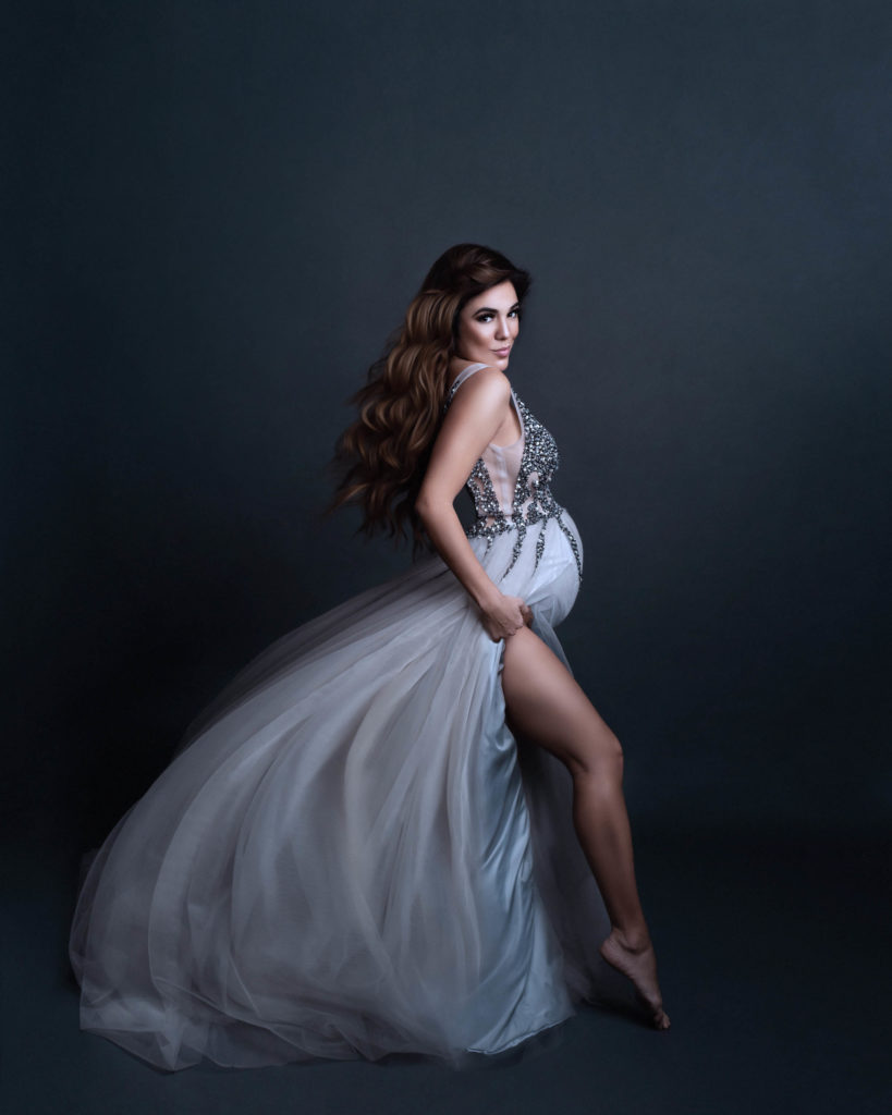 Pregnant dancer with long wavy hair is wearing a formal lavender gown with sequins for maternity picture outfit ideas
