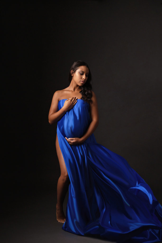 Woman drapes blue fabric over her baby bump during a maternity photoshoot