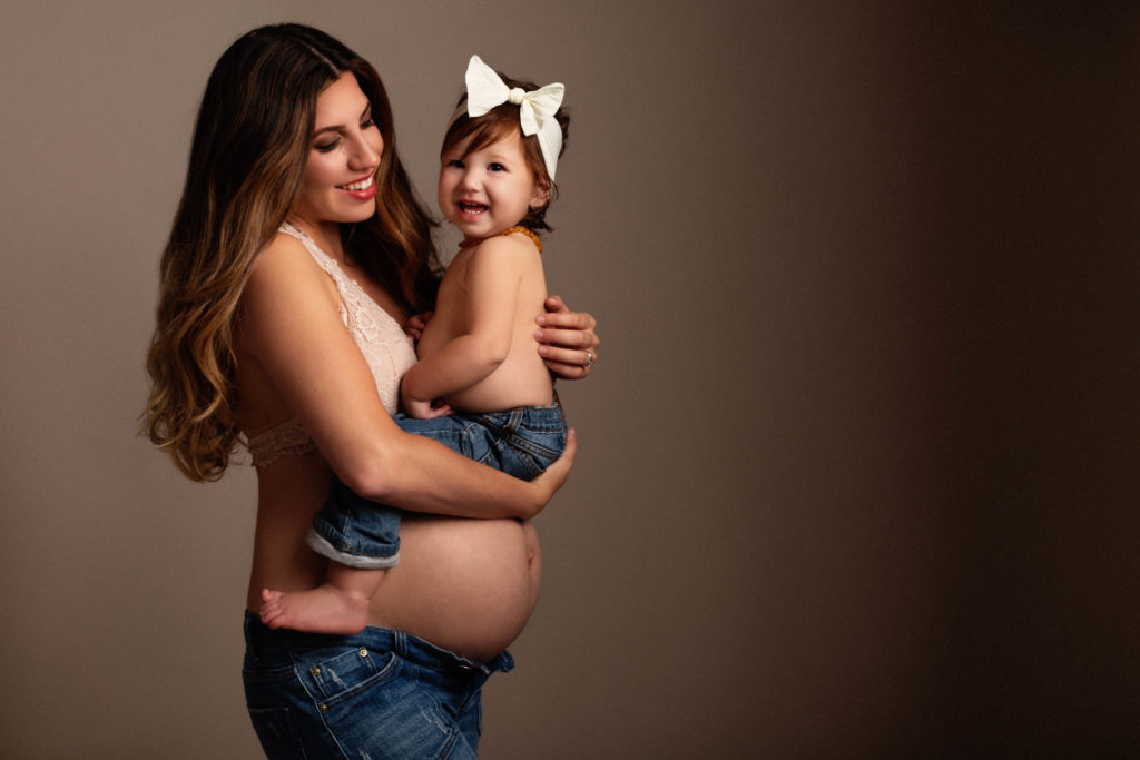 Pregnant mom holding toddler daughter in her arms while laughing together during pregnancy photography photoshoot