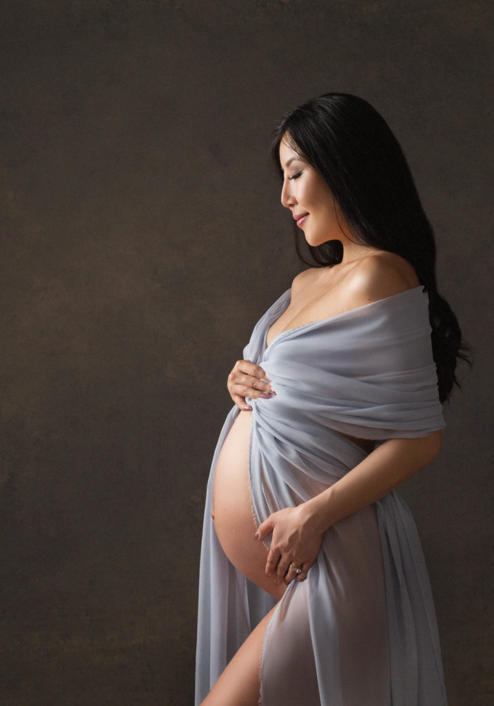pregnant mom smiles sweetly while draped in lavender fabric during maternity photoshoot