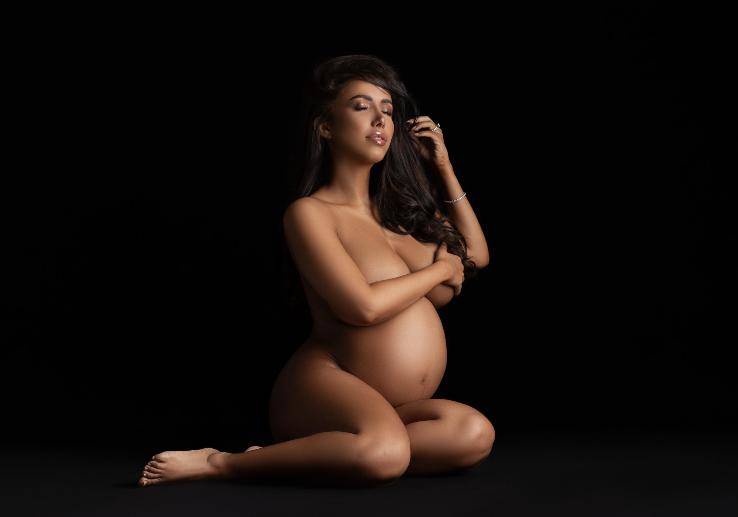 nude pregnant woman sitting on black background