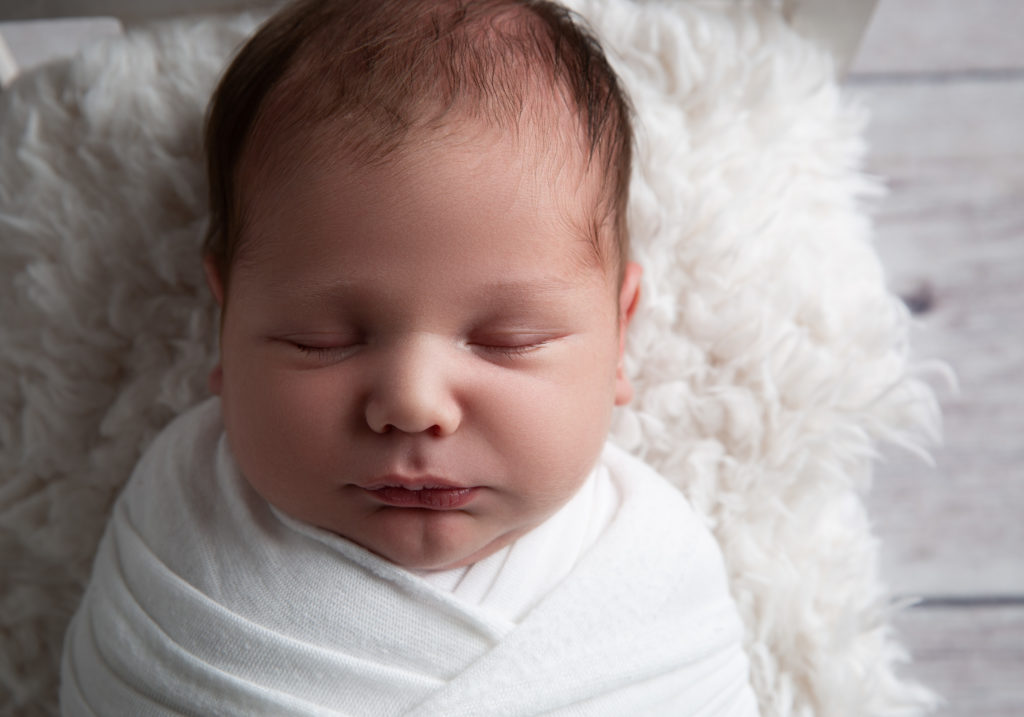 close up of newborn baby boy wrapped in white