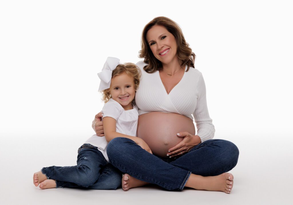 pregnant woman and daughter sitting posing in all white