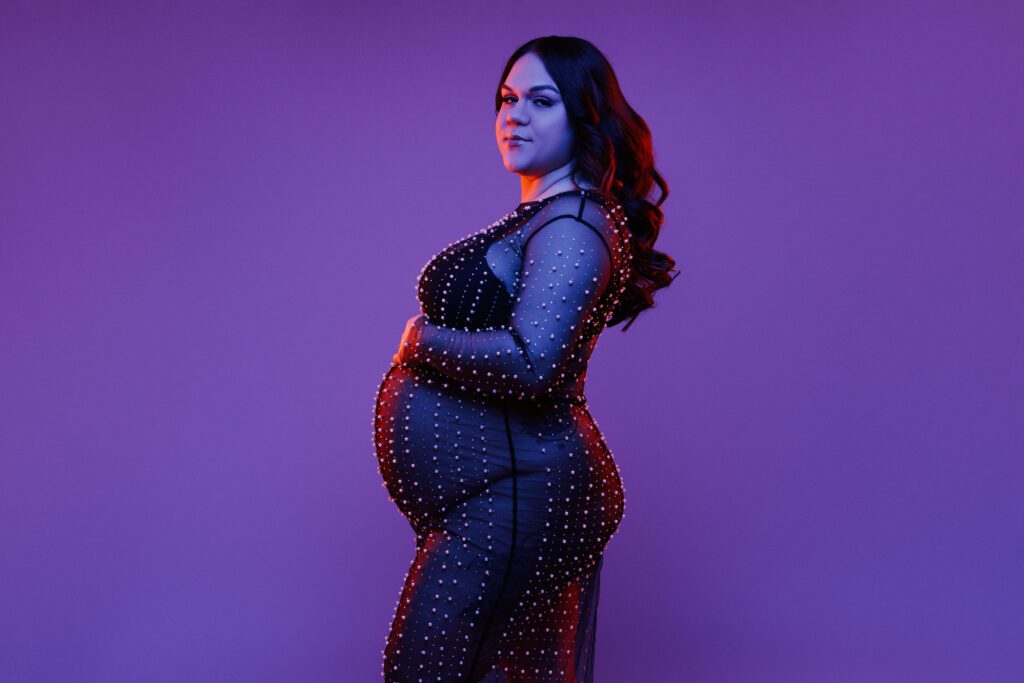 maternity shoot of woman in black sparkly dress with colorful lighting