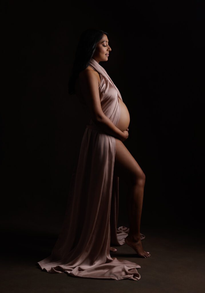 pregnant woman with rose colored silk wrapped around with black back drop