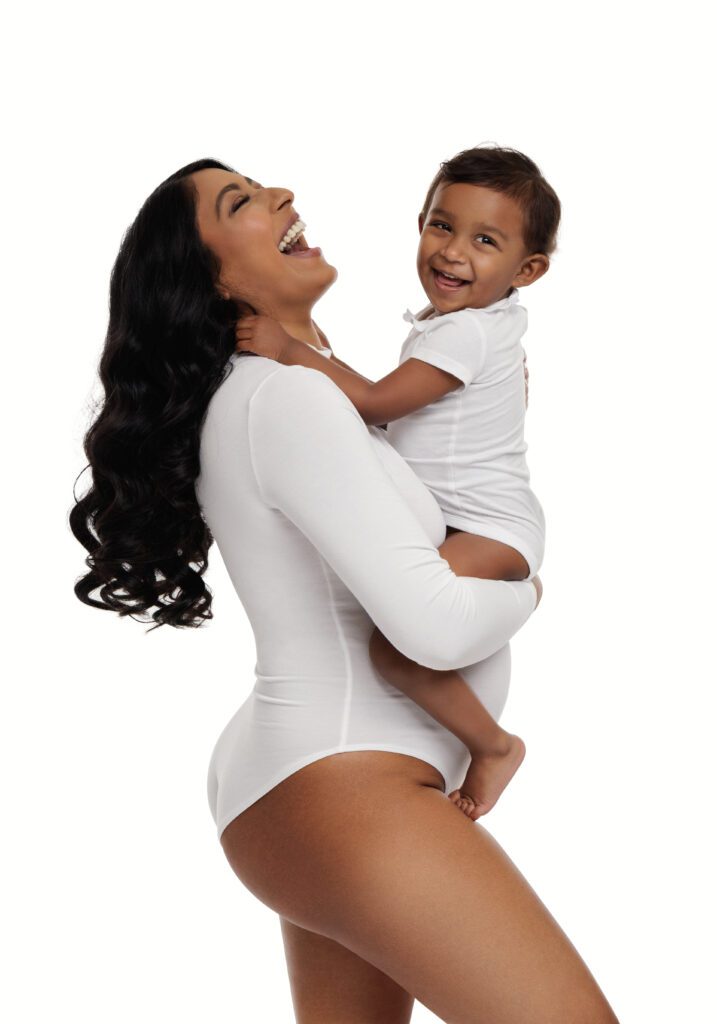 pregnant woman wearing white bodysuit while holding her child 