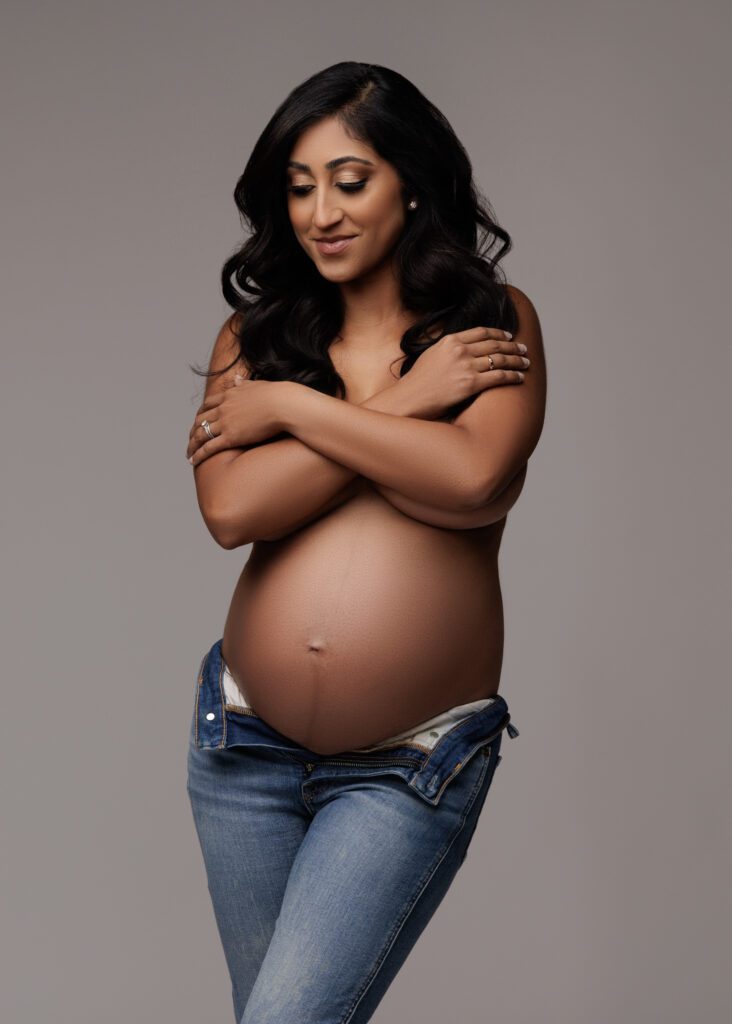 maternity shoot of woman in jeans with grey backdrop
