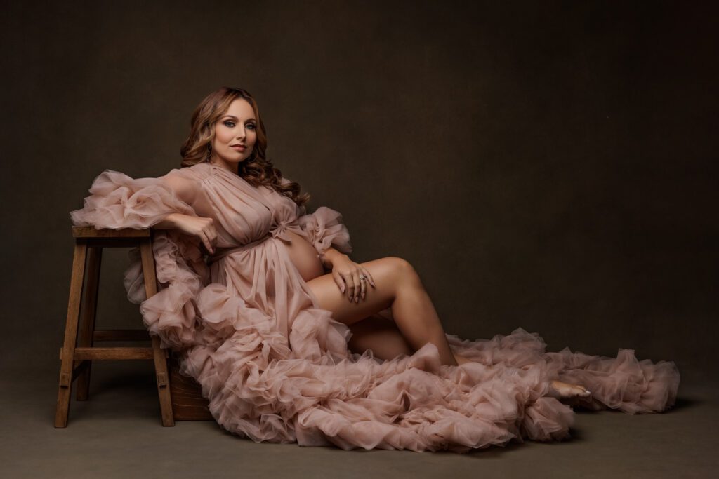 Pregnant woman in flowing blush tulle gown posed in studio during luxury maternity photography session in Miami